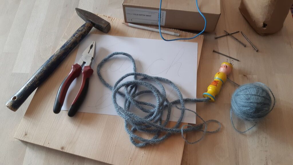 Strickliesel, Wolle, Kabel oder Draht, Nägel, Hammer und Zange, Holzbrett, Papier und Bleistift ist alles was man für den DIY Schriftzug aus Wolle braucht.