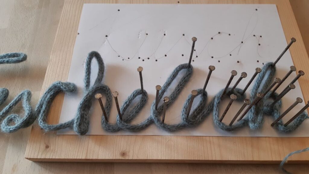 Der mit dem Kabel gefüllte Strickschlauch wird um die Nägel in From gebogen.