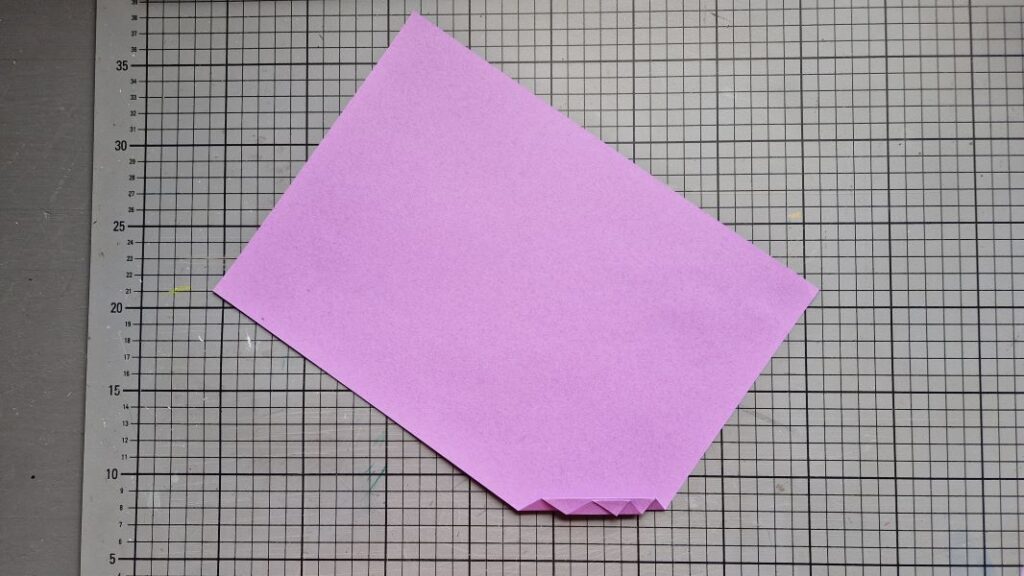 Ein Blatt violettes Buntpapier das von unten zur Ziehharmonika gefaltet wird.