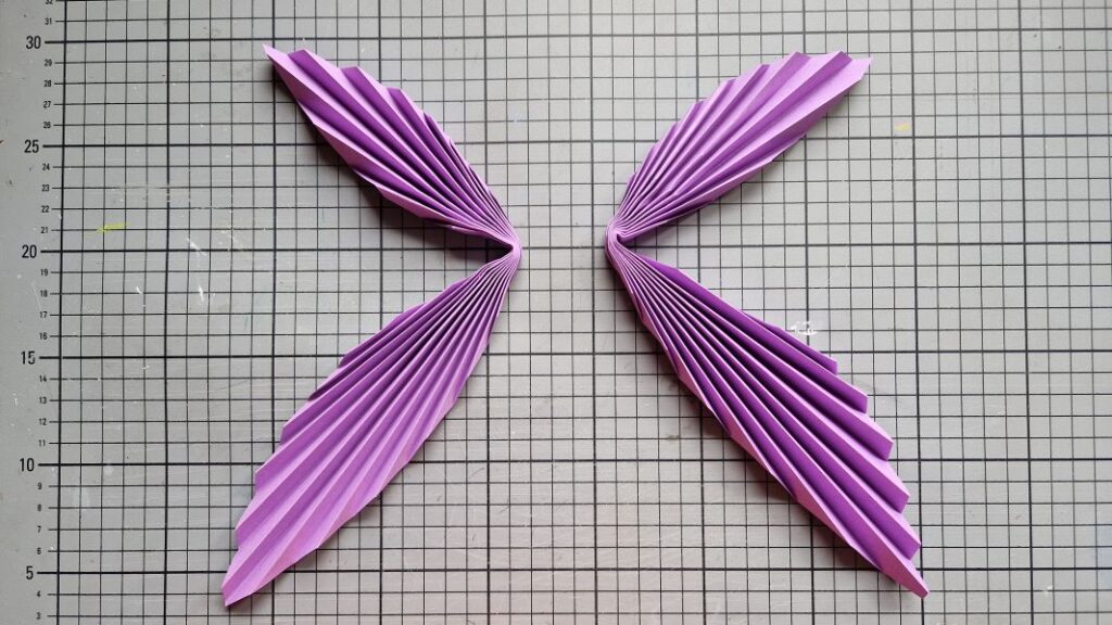 Zwei Blätter violettes, zur Ziehharmonika gefaltetes Buntpapier, von denen eines nach links und eines nach rechts geknickt ist.