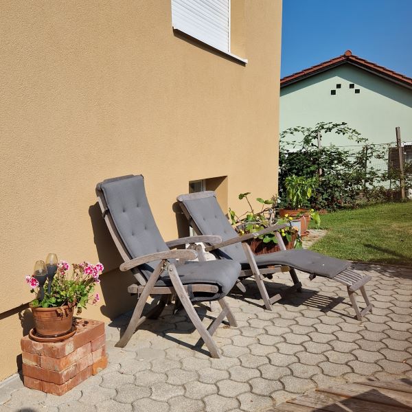 Terrasse mit Sonnenliegen aus Holz die vor einer Hauswand stehen und von Topfpflanzen umgeben sind.