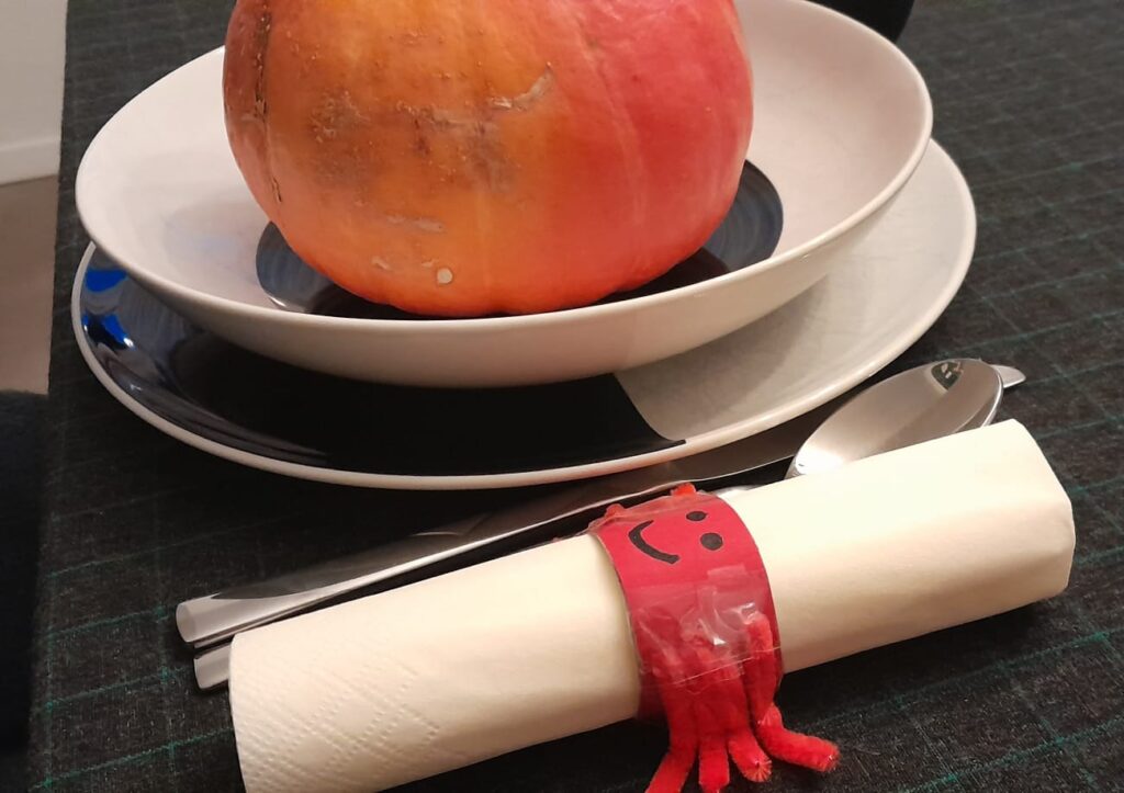 Ein schwarzes Tischtuch mit grünem Karo, schwarz-weißes Geschirr, schwarz-goldene Trinkbecher und der DIY Spinnen-Serviettenring machen Lust auf eine Halloween Party.