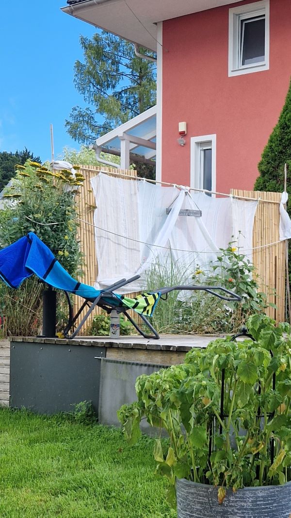 Zwei Bambusmatten sind mit Eisenstangen stabil im Blumenbeet verankert und halten eine Querstange für die transparenten Vorhangbahnen. Der Sichtschutz ist so auch windsicher.